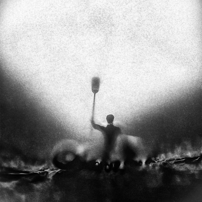 Homme sur radeau qui lève sa rame devant le phare colossal qui s’avance vers lui. Image de synthèse 3D, noir et blanc.